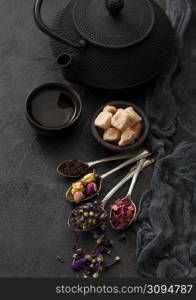 Chinese teapot with cup and spoons with various tea on black. Rose buds,blue mallow flowers,green and black loose tea