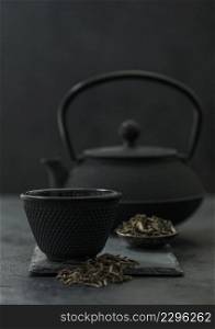 Chinese teapot with plate of loose black tea and cup on black .