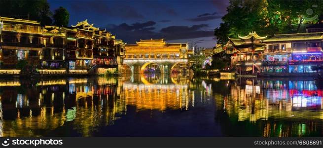 Chinese tourist attraction destination - panorama of Feng Huang Ancient Town  Phoenix Ancient Town  on Tuo Jiang River illuminated at night. Hunan Province, China. Feng Huang Ancient Town  Phoenix Ancient Town  , China