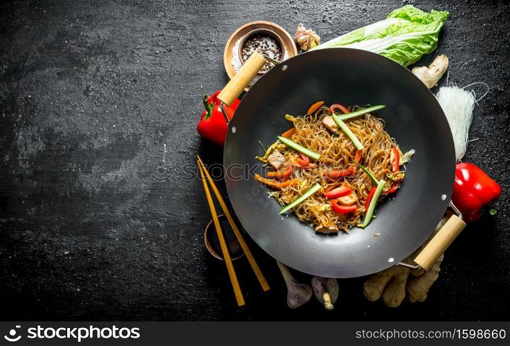 Chinese wok. Ready funchoza noodles with vegetables and ingredients for its preparation. On black rustic background. Chinese wok. Ready funchoza noodles with vegetables and ingredients for its preparation.
