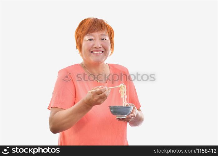 Chinese woman eating with chopsticks looking and smiling to camera, on a light background.