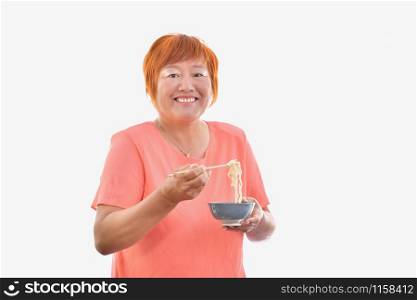 Chinese woman eating with chopsticks looking and smiling to camera, on a light background.