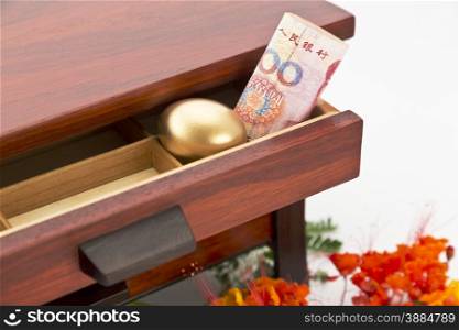 Chinese yuan currency and gold nest egg nestled in wood drawer