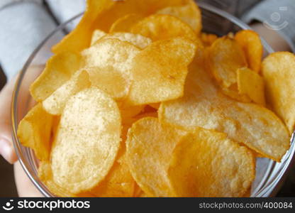 Chips close-up, in a glass container. A child holds a bunch of yellow chips. Junk food.. Chips close-up, in a glass container. A child holds a bunch of yellow chips.