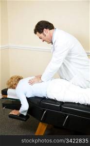 Chiropractor adjusting a woman&rsquo;s spine as she lays on the examining table.
