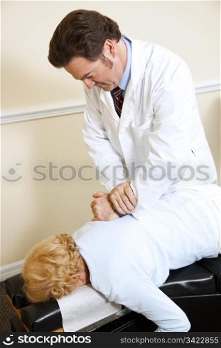 Chiropractor gives a spinal adjustment to a senior woman.