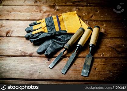 Chisel with construction gloves on the table. On a wooden background. High quality photo. Chisel with construction gloves on the table.