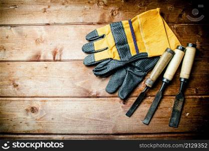 Chisel with construction gloves on the table. On a wooden background. High quality photo. Chisel with construction gloves on the table.