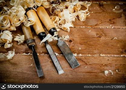 Chisels with wooden shavings. On a wooden background. High quality photo. Chisels with wooden shavings. On a wooden background.