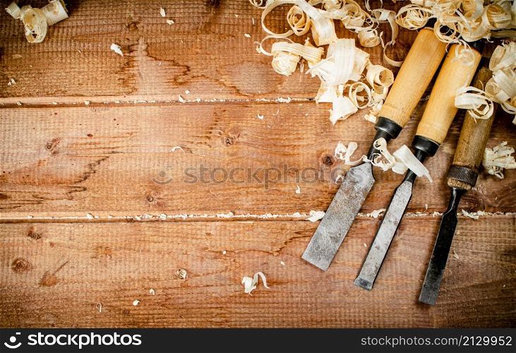 Chisels with wooden shavings. On a wooden background. High quality photo. Chisels with wooden shavings. On a wooden background.