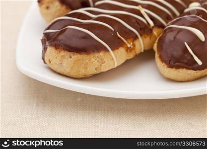 choclate eclair pastry on white plate against tablecloth, shallow depth of field
