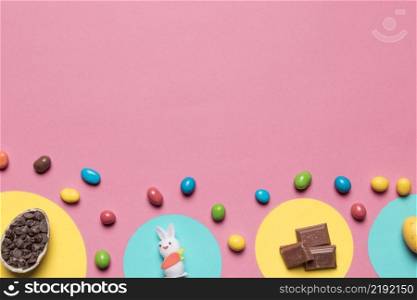 choco chips rabbit statue chocolate pieces colorful candies pink backdrop with space text