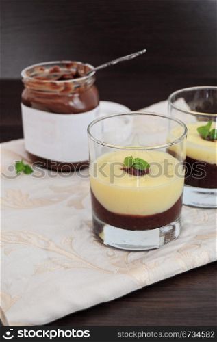 Chocolate and vanilla cream, served in glasses, jar of chocolate spread in the background