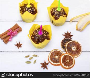 chocolate banana muffins with a candle on a white wooden background, top view
