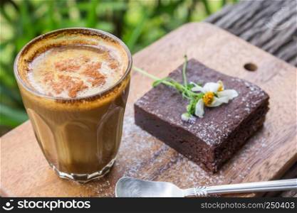Chocolate Brownie Cake and Latte Coffee and Daisy Flower on Chopping Board or Cutting Board on Wood Table on Green Tree Background Top Frame.