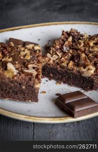 Chocolate brownie with walnuts portion and a piece of chocolate, on a plate.
