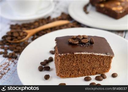 Chocolate cake on a white plate and coffee beans on a wooden spoon on a wooden table