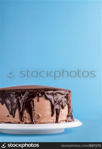Chocolate cake with dripping melted chocolate on a blue background. Colorful birthday cake frame. Homemade chocolate dessert. Chocolate glazed cake.