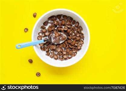 Chocolate cereal with milk on yellow background. Top view