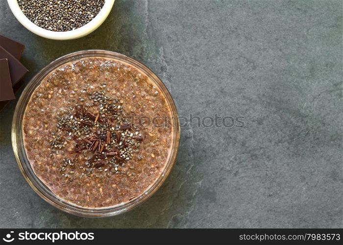 Chocolate chia seed pudding in glass bowl with chia seeds and chocolate shavings on top, photographed overhead on slate with natural light