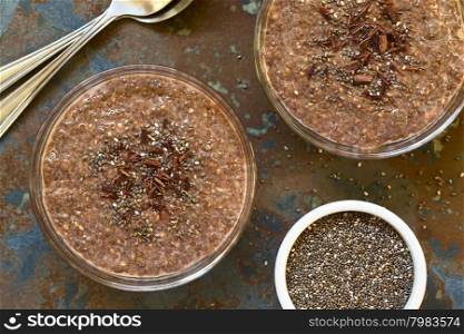 Chocolate chia seed pudding in glass bowls with chia seeds and chocolate shavings on top, photographed overhead on slate with natural light