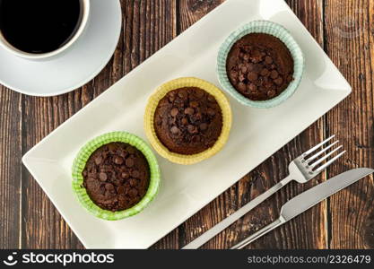 Chocolate chip and cocoa muffins in colorful muffin paper molds on wooden table
