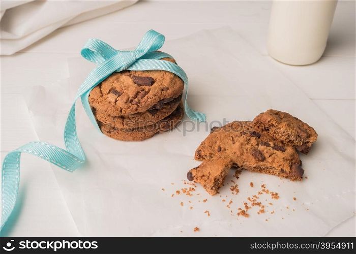 Chocolate chip cookies with a blue ribbon and a glass of milk on a white wooden table background. Vintage look.