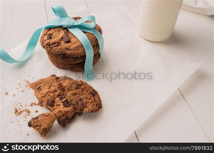 Chocolate chip cookies with a blue ribbon and a glass of milk on a white wooden table background. Vintage look.