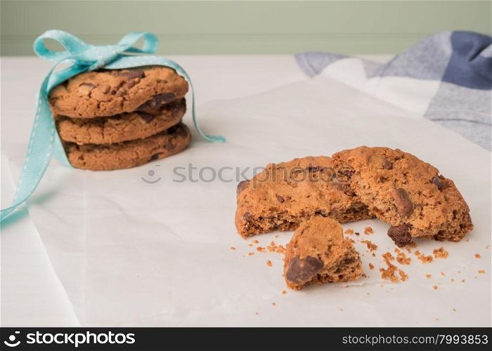 Chocolate chip cookies with a blue ribbon and a glass of milk on a white wooden table with a robin egg blue background. Vintage look.