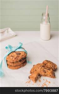 Chocolate chip cookies with a blue ribbon and a glass of milk with a straw on a white wooden table with a robin egg blue background. Vintage look.