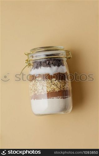 Chocolate chips cookie ingredients in glass jar on color paper background, flat lay