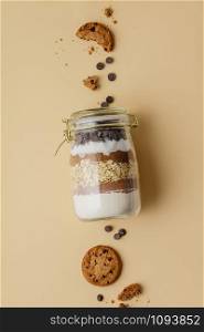Chocolate chips cookie ingredients in glass jar on color paper background, flat lay