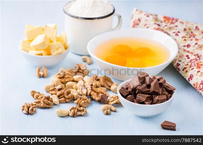 Chocolate chunks, eggs, butter, nuts and cup of flour. Ingredients for baking. Selective focus