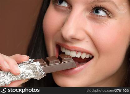 Chocolate - close-up of young woman bite sweets on brown background