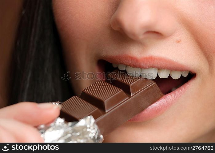 Chocolate - close-up of young woman bite sweets on brown background