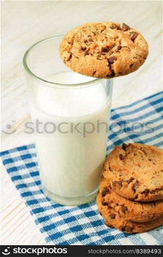 Chocolate cookie and glass of milk on blue napkin on white wooden table. Dairy product concept. Chocolate cookie and glass of milk