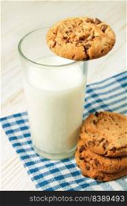 Chocolate cookie and glass of milk on blue napkin on white wooden table. Dairy product concept. Chocolate cookie and glass of milk
