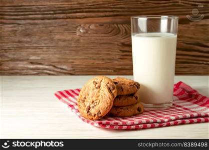 Chocolate cookie and glass of milk on red napkin on brown wooden table. Dairy product concept, copy space for text. Chocolate cookie and glass of milk