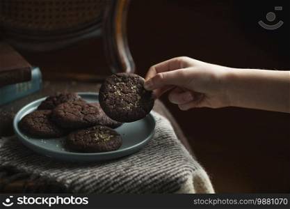 Chocolate cookies on the plate. Dark and Moody, Mystic Light food photography. Children’s hand takes a cookie from the plate.