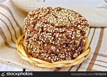 Chocolate cookies with sesame seeds in a wicker plate, napkin on a lighter background of the board