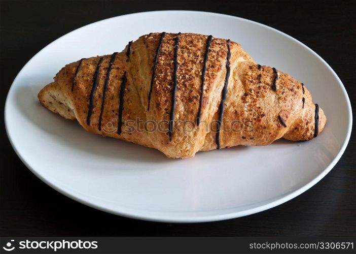 Chocolate croissant on white plate standing on dark wooden table