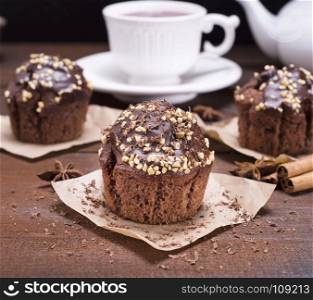 chocolate cupcakes with walnut on a brown wooden background, behind a white cup of tea