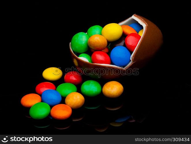 Chocolate egg with colorful small round candies on black background