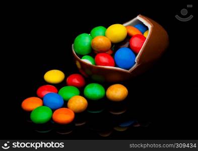 Chocolate egg with colorful small round candies on black background