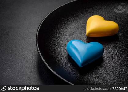 Chocolate hearts in the colors of the Ukrainian flag on a black ceramic plate. Valentine’s day in Ukrainian colors