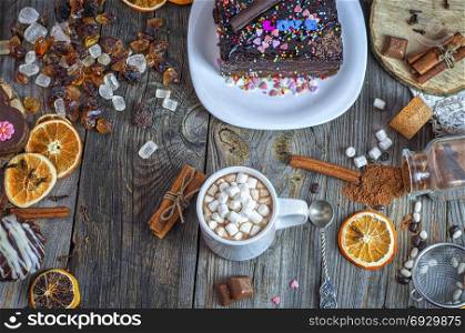 Chocolate in a cup with marshmallow, top view, the table is made with different sweets and a piece of chocolate cake