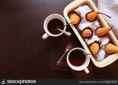 Chocolate loaf cake with whole pears baked inside and two cups coffee on dark background. Top view .. Chocolate loaf cake with whole pears baked inside and two cups coffee on dark background. Top view