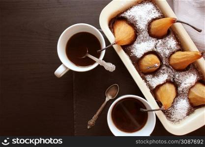 Chocolate loaf cake with whole pears baked inside and two cups coffee on dark background. Top view .. Chocolate loaf cake with whole pears baked inside and two cups coffee on dark background. Top view