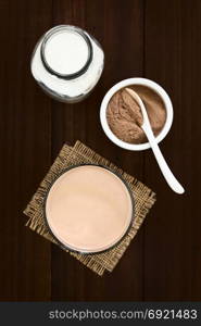 Chocolate milk drink in glass, bottle of milk and chocolate or cocoa powder on the side, photographed overhead with natural light (Selective Focus, Focus on the chocolate drink). Chocolate Milk Drink