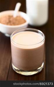 Chocolate milk drink in glass, chocolate or cocoa powder and milk in the back, photographed with natural light (Selective Focus, Focus on the front of the glass rim). Chocolate Milk Drink